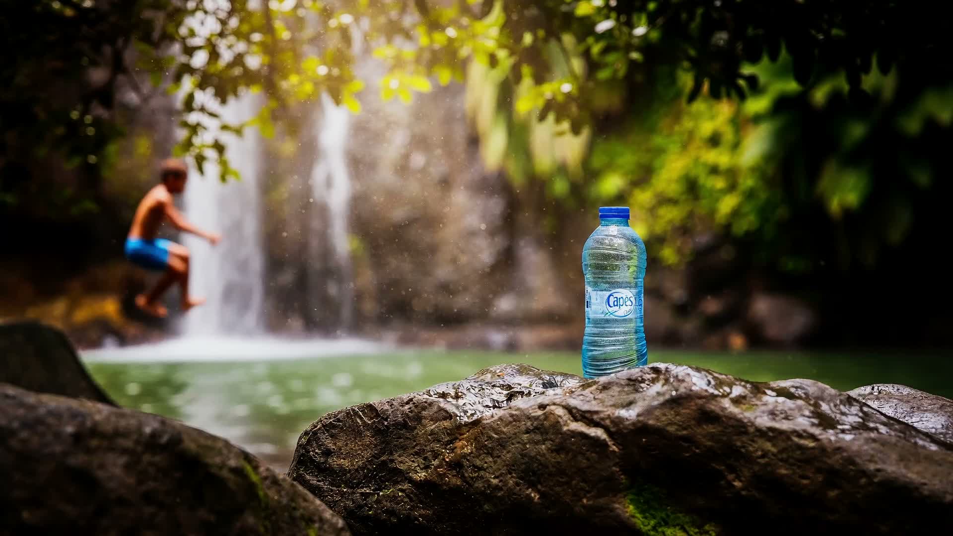 Une bouteille Capès devant une cascade en pleine nature